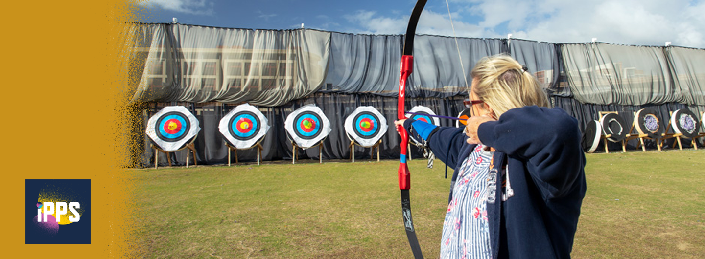 IPPS logo and image of ipps staff member taking aim with a bow and arrow  the UC San Diego archery field
